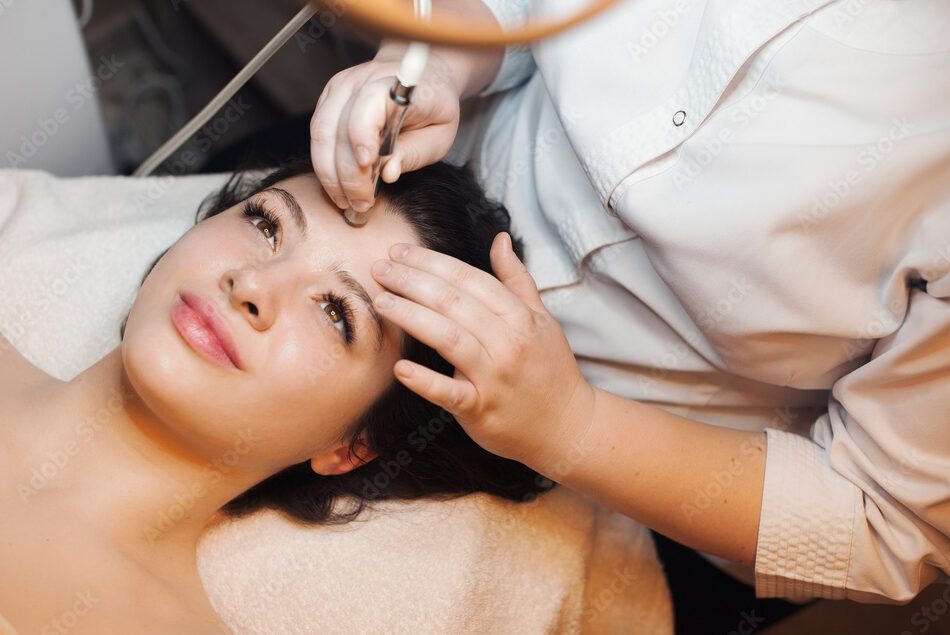 Upper view of a lovely caucasian female having a facelift procedures on her face leaning on a spa bed with open eyes .